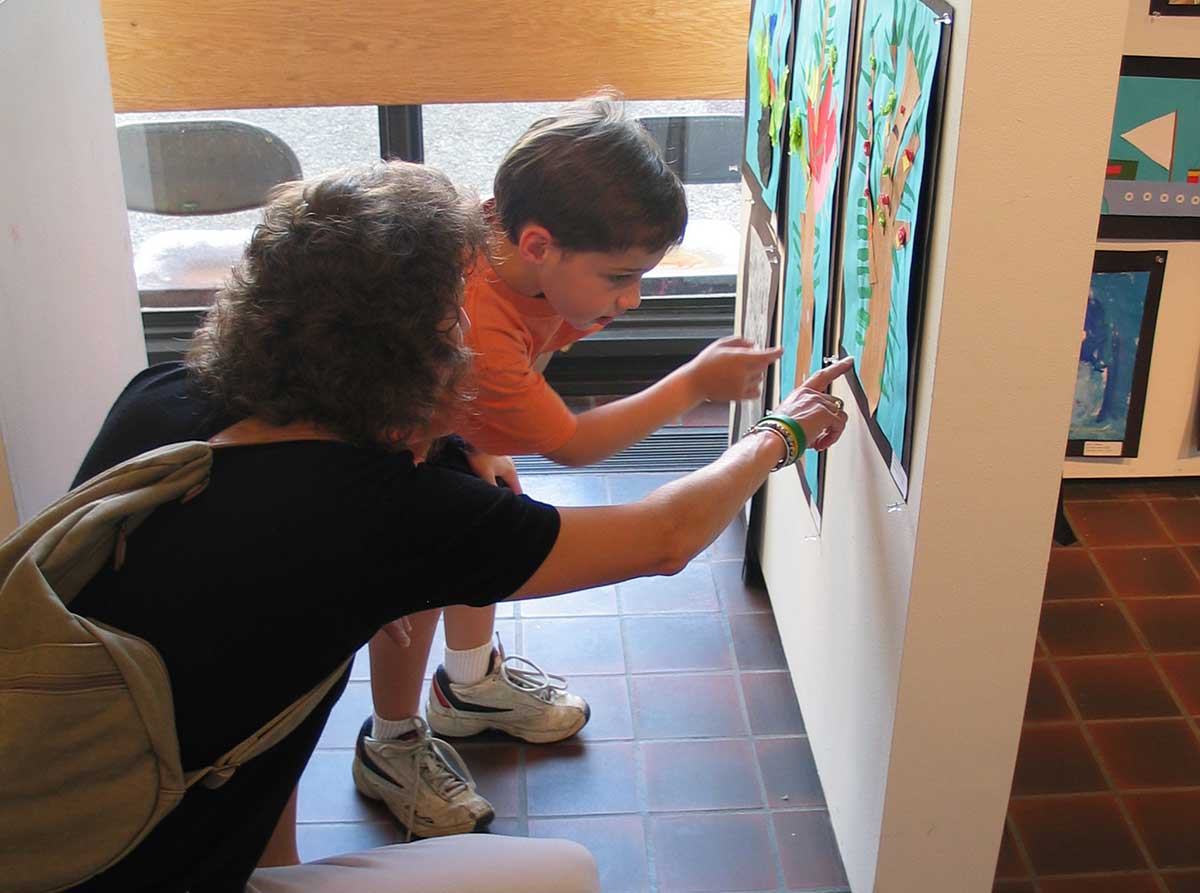 A small boy and his mother crouch down to examine (his?) artwork on during a Youth CLasses exhibition opening
